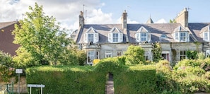 A row of stone houses with multiple chimneys, surrounded by lush greenery and a clear sky.