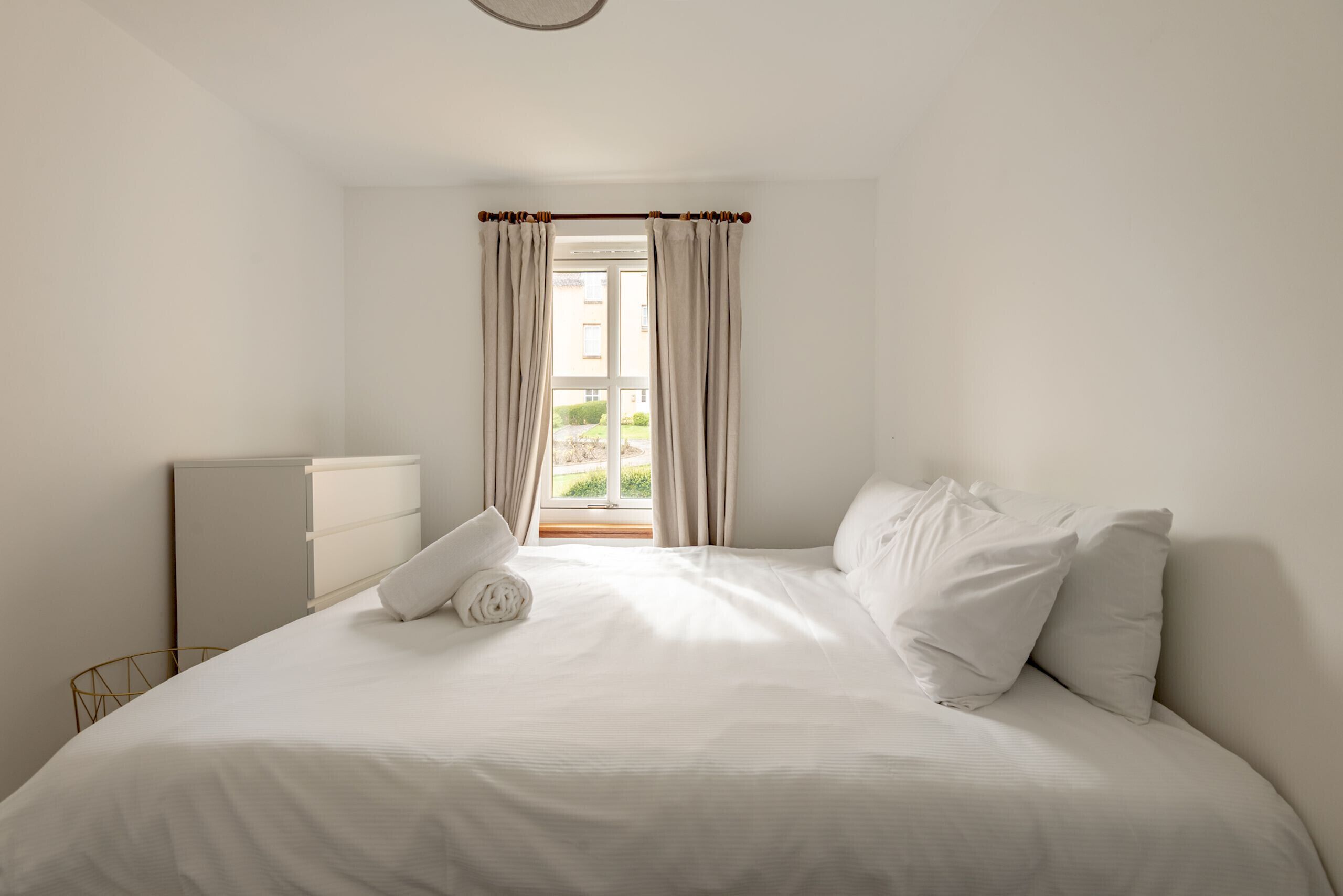 A bedroom with a bed, pillows, a bedside table, and a window with curtains.