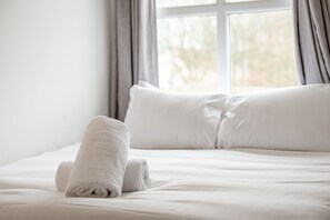 A neatly made bed with white linens and a rolled white towel on the side. - Bobby Jones Apartments (No 42) (St Andrews)