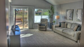 Ein Wohnzimmer mit Sofa, Sessel und Couchtisch. Ein Fenster bietet Blick auf ein Haus und eine Pflanze.