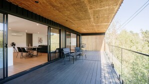 A modern outdoor balcony with a wooden deck, glass doors leading to an interior dining area, and a view of trees. - Tree Top Treasure ITAS (South Launceston)