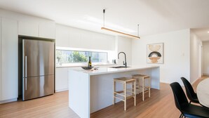 A modern kitchen with a large island, stainless steel refrigerator, and wooden stools. - Tree Top Treasure ITAS (South Launceston)