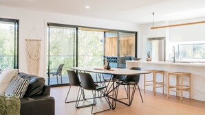 A modern kitchen with a dining area, large windows, and a macrame wall hanging. - Tree Top Haven ITAS - Hosted by L'Abode (South Launceston)