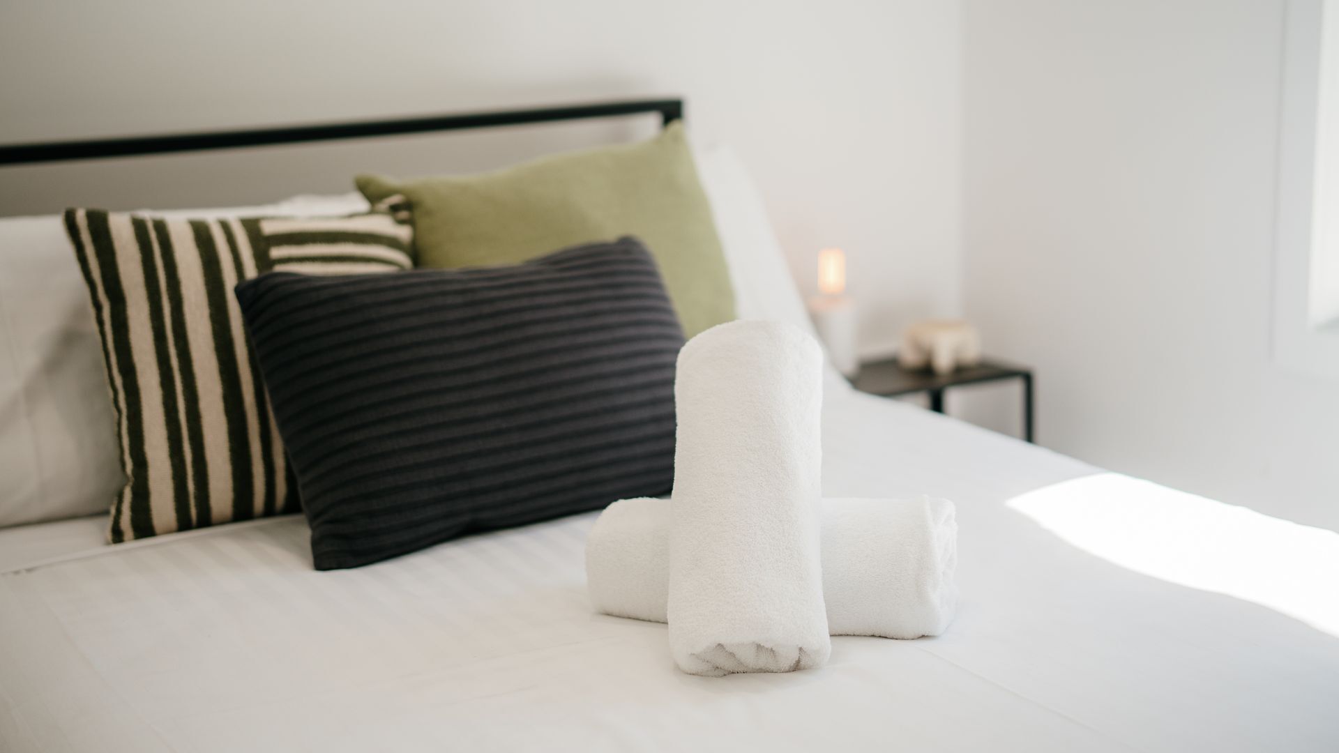 Una cama bien hecha con ropa blanca, almohadas a rayas y una almohada verde.
