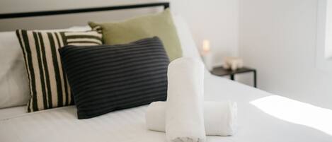 Una cama bien hecha con ropa blanca, almohadas a rayas y una almohada verde.
