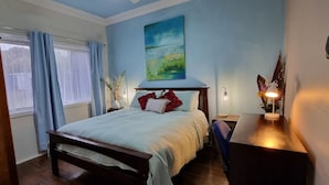 A bedroom with a bed, a nightstand, a window with curtains, a painting on the wall, and a wooden wardrobe.