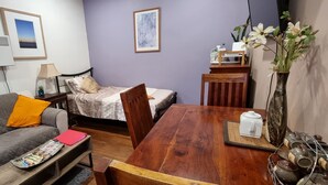 A cozy room with a grey couch, a wooden dining table, and a bed with a white bedspread.