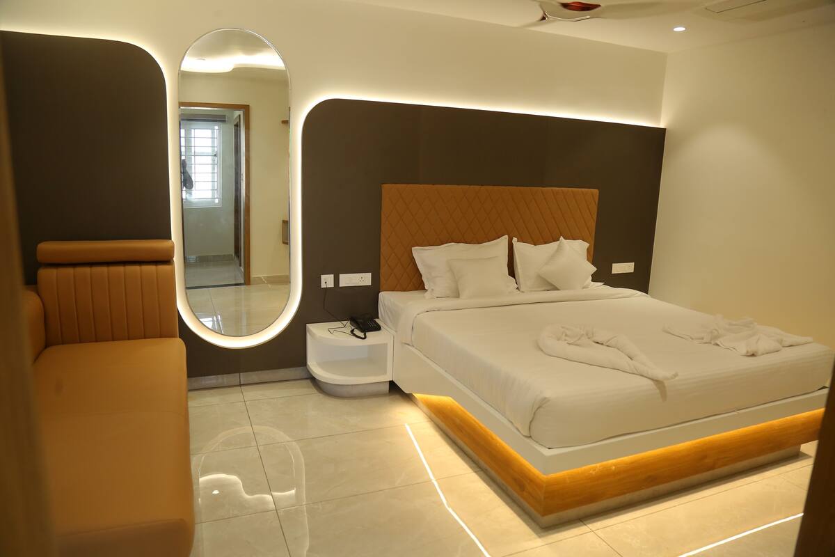 Una habitación de hotel moderna con una cama grande, una mesita de noche, un espejo y un área de descanso.