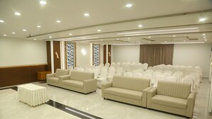 A spacious conference room with a long table, two sofas, and rows of chairs. - SRIPADAM GRAND (Chilakaluripet)