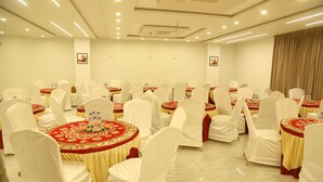 A banquet hall with round tables covered in red and gold tablecloths, white chairs, and a tiled floor. - SRIPADAM GRAND (Chilakaluripet)