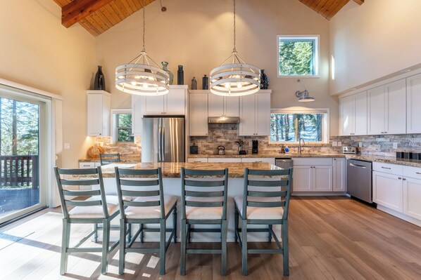A spacious kitchen with a large island, white cabinetry, and a wooden ceiling.