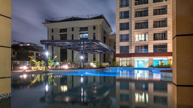 A hotel pool area with a covered seating area, a reflection pool, and a building with multiple floors and balconies. - Kilimani Bliss,Alba gardens studio apartment with a gym, infinity swimming pool (Nairobi)