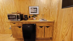 Eine kompakte Küche mit Mikrowelle, Kaffeemaschine, Spüle und kleinem Kühlschrank.