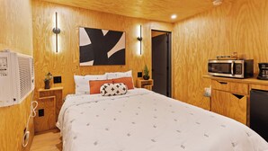 Ein Hotelzimmer mit Holzvertäfelung, einem Bett mit gemustertem Überwurf, einer Mikrowelle, einer Kaffeemaschine und einer wandmontierten Klimaanlage.