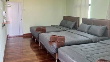 Een hotelkamer met twee bedden, een houten vloer, een witte deur, een airconditioning en een raam met gordijnen.