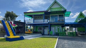 A two-story building with a green and white facade, a balcony, and a small outdoor seating area with green plastic chairs. - Baan Thammarot View (Sirindhorn)