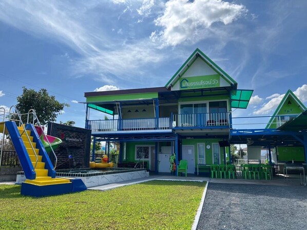 A two-story building with a green and white facade, a balcony, and a small outdoor seating area with green plastic chairs. - Baan Thammarot View (Sirindhorn)
