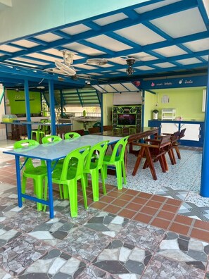 A covered outdoor dining area with a blue ceiling, green plastic chairs, and a tiled floor. - Baan Thammarot View (Sirindhorn)