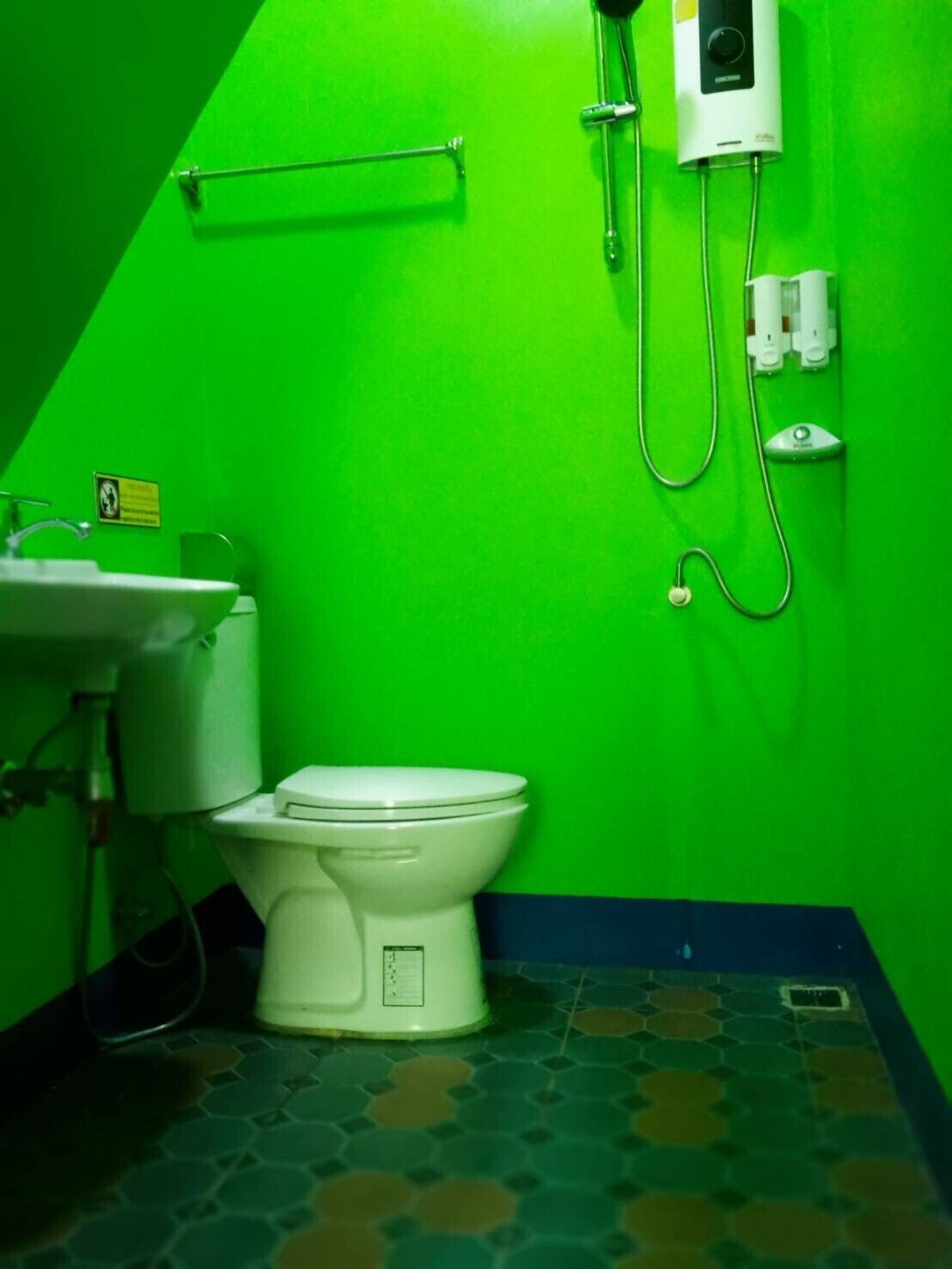 A bathroom with a green wall, a white toilet, a sink, and a shower with a control panel.