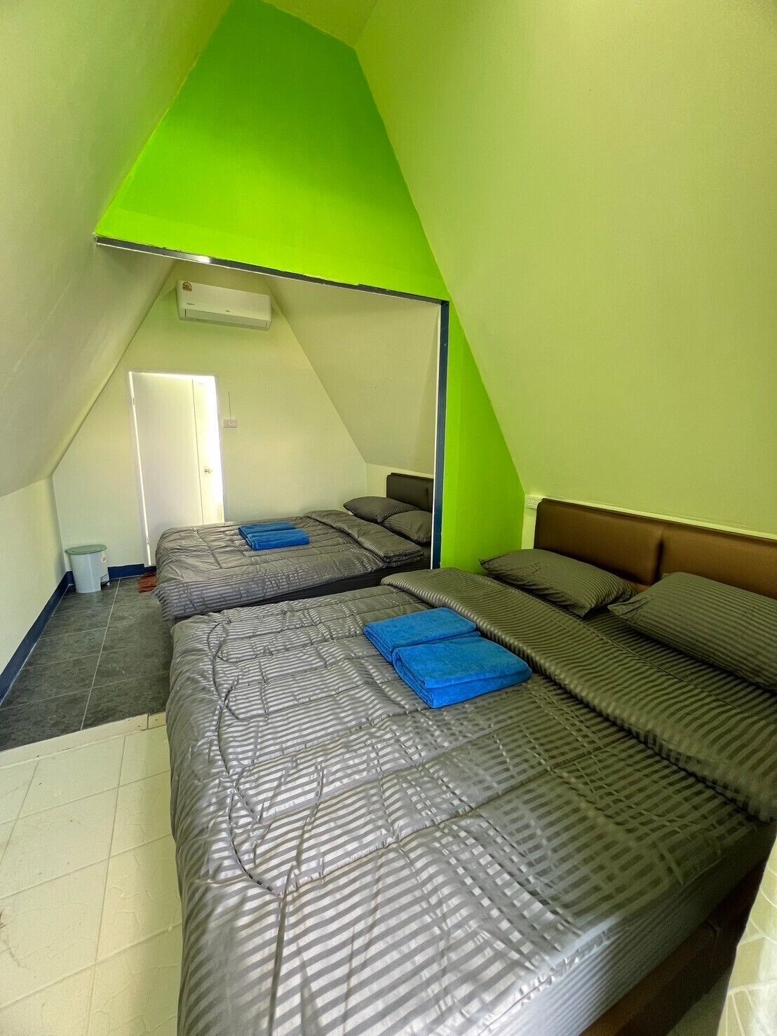 Un pequeño dormitorio en ático, de forma triangular, con dos camas, techo inclinado verde y una puerta blanca.