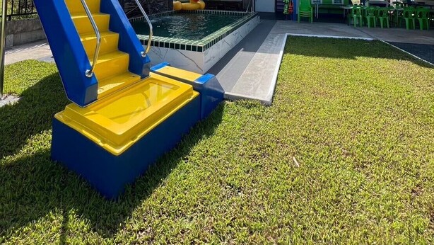 A building with a swimming pool, a staircase with blue and yellow steps, and a green roof. - Baan Thammarot View (Sirindhorn)