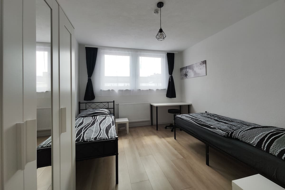 Quarto com cama, escrivaninha e janela.