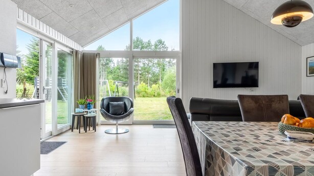 A modern living room with a large window, a dining area with a patterned tablecloth, and a black leather chair.