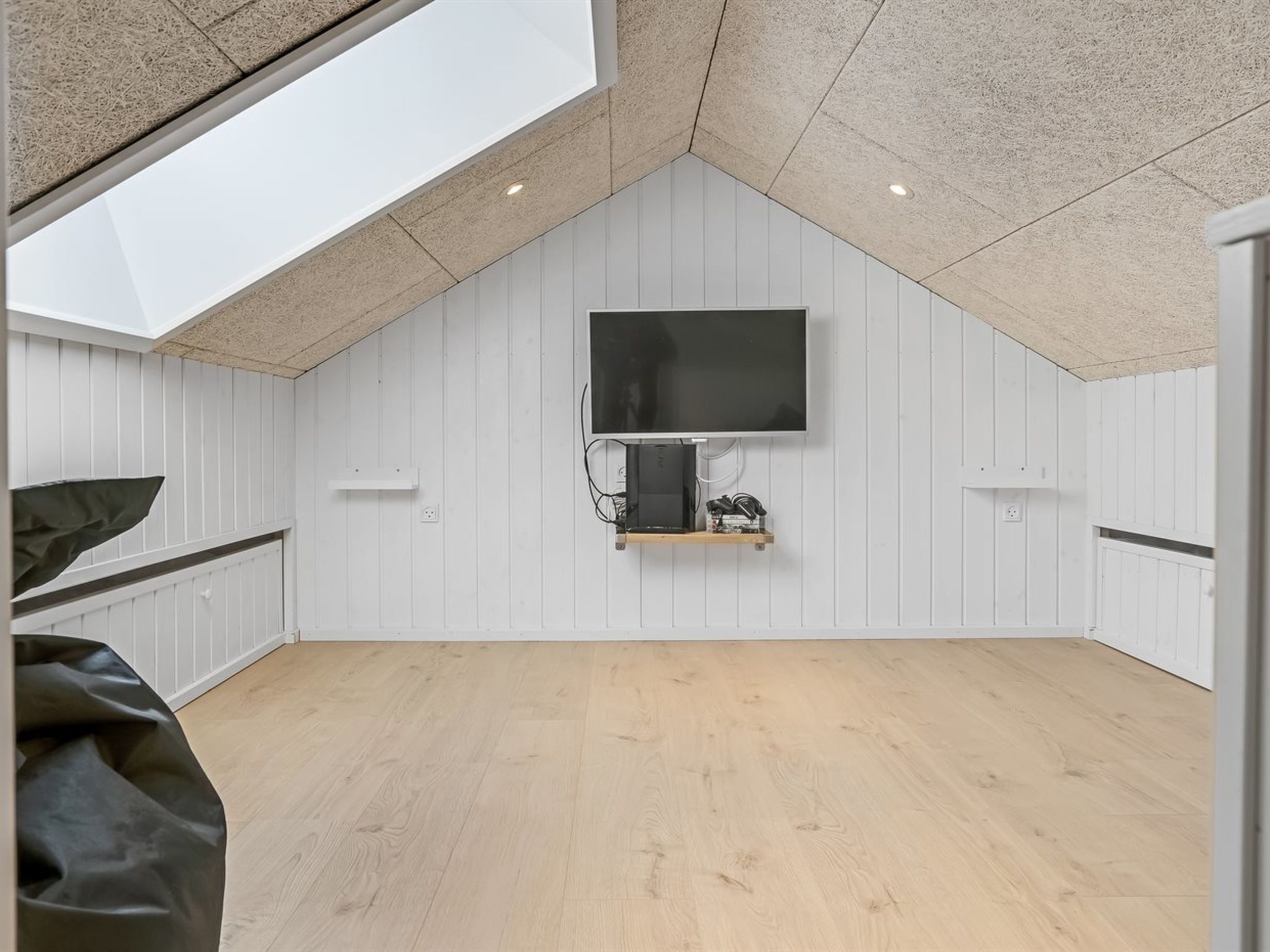 Una habitación con techo inclinado, televisor montado y piso de madera.
