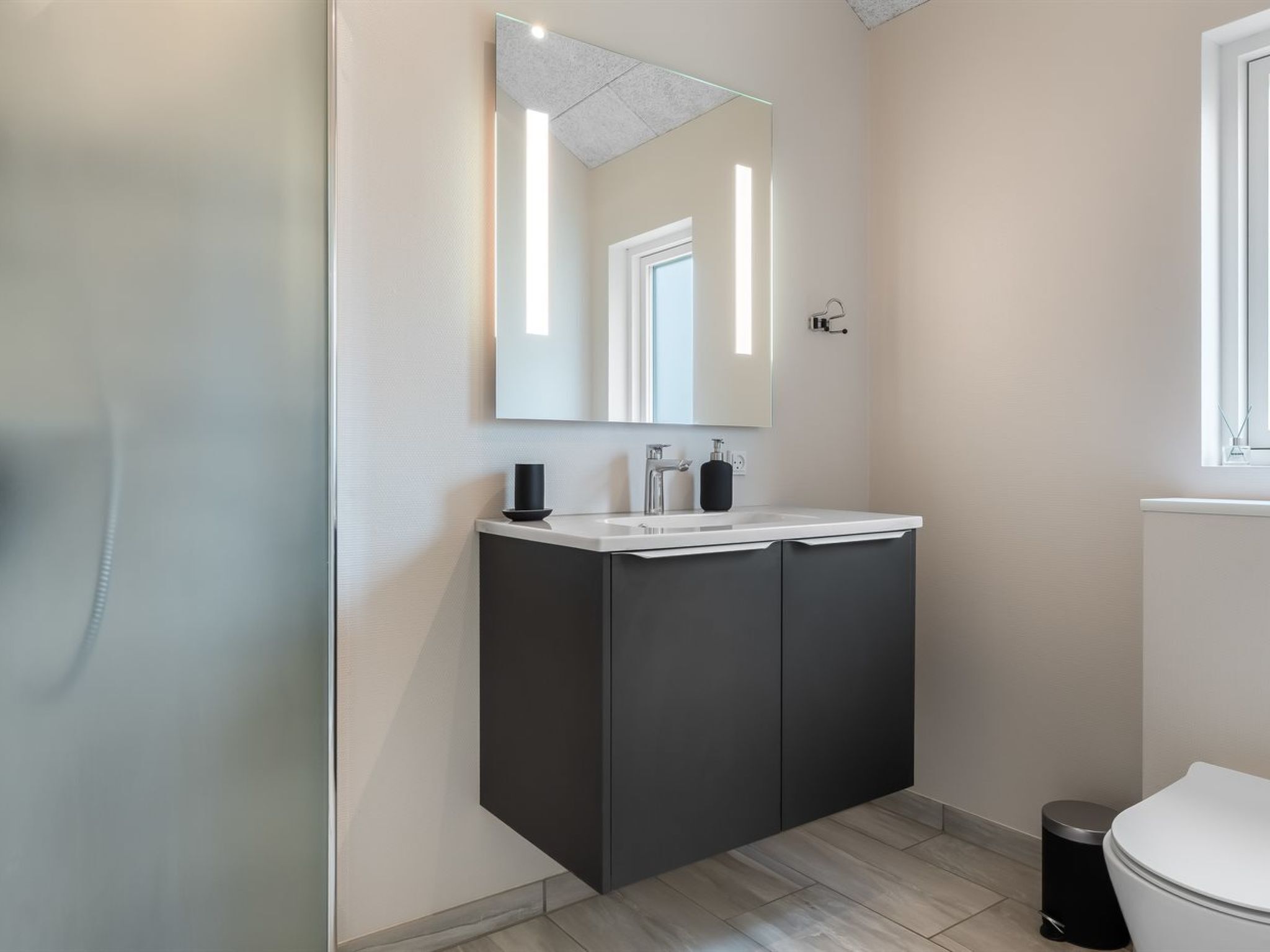 Ein modernes Badezimmer mit einem weißen Waschbecken, dunklen Schränken und einem großen Spiegel.