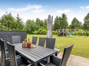 Un área de comedor al aire libre con una mesa y sillas, una estructura de juegos para niños y una valla de madera.