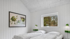 A bedroom with a bed, white walls, a framed picture, a window with a view, and two bedside lamps.