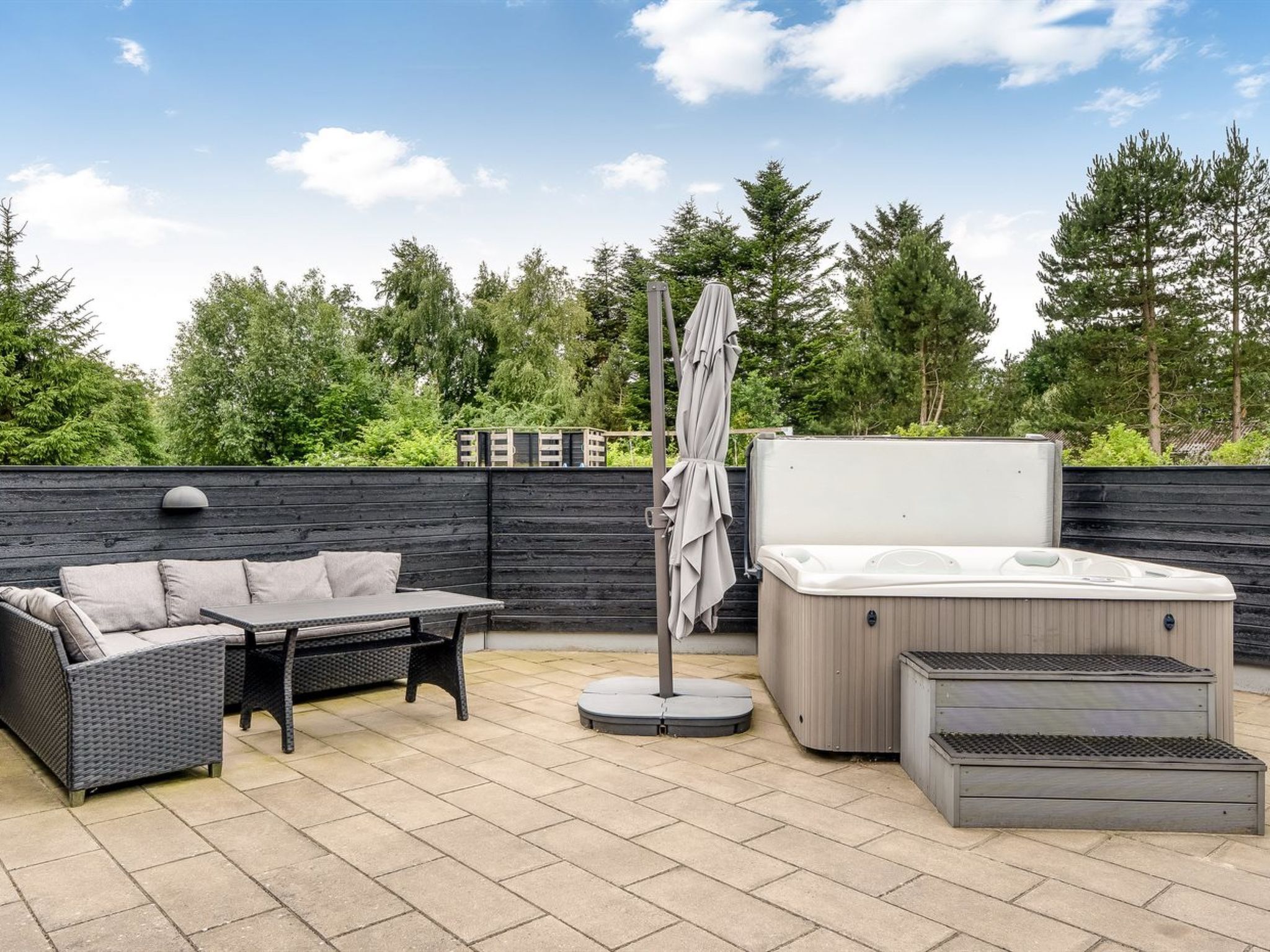 Een terras met een bank, een tafel, een jacuzzi en een overdekte parasol.