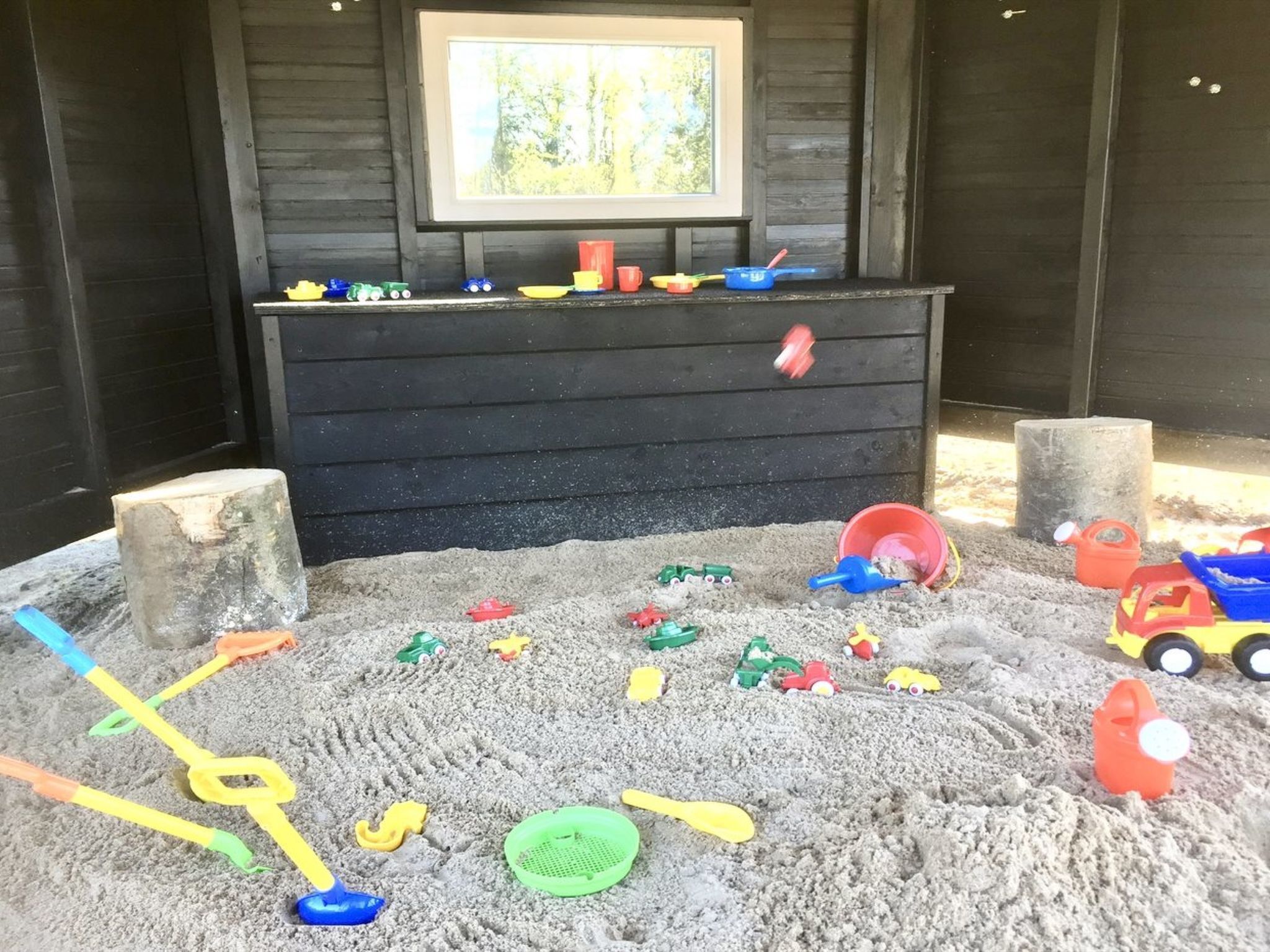 Zona infantil con arena, juguetes y un aparador negro.