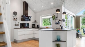 A modern kitchen with white cabinetry, a central island, a built-in stove, and a window providing a view of greenery outside.