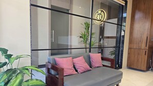 A modern interior with a grey sofa, wooden cabinet, and large windows. - Hotel Elite (Bhachau)