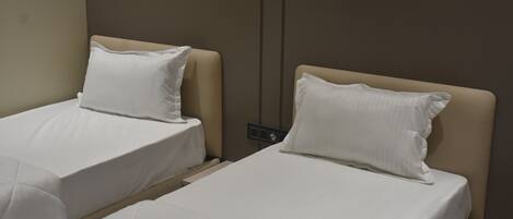 Two single beds with white linens and headboards, a neutral wall color, and a visible electrical outlet.