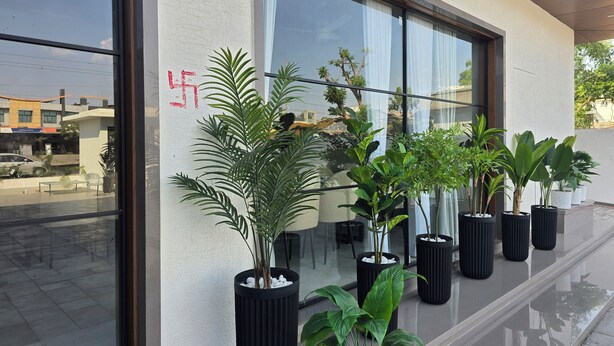A modern building exterior with large windows, potted plants, and a clear view of the street outside. - Hotel Elite (Bhachau)