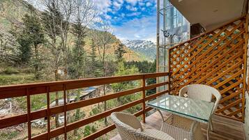 A balcony with wicker furniture and a glass table, overlooking a mountainous landscape.
