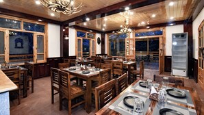 Un restaurante con mesas y sillas de madera, un candelabro y ventanas amplias.