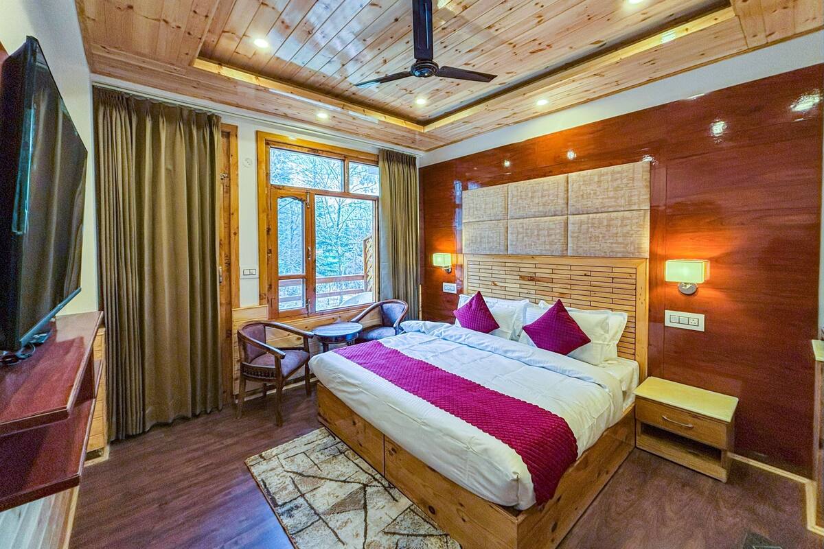Habitación de hotel con techo de madera, cama con colcha roja y blanca, escritorio con silla y televisor.