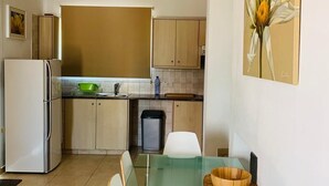 A modern kitchen with a glass dining table, white chairs, and a painting of a flower on the wall.