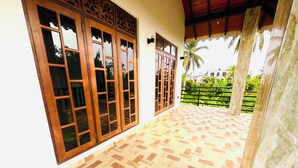 A covered outdoor area with patterned flooring, large wooden-framed windows, and a view of greenery. - 5-bedroom villa in wonderful Negombo, 10 mins away from Airport & Beach. (Negombo)