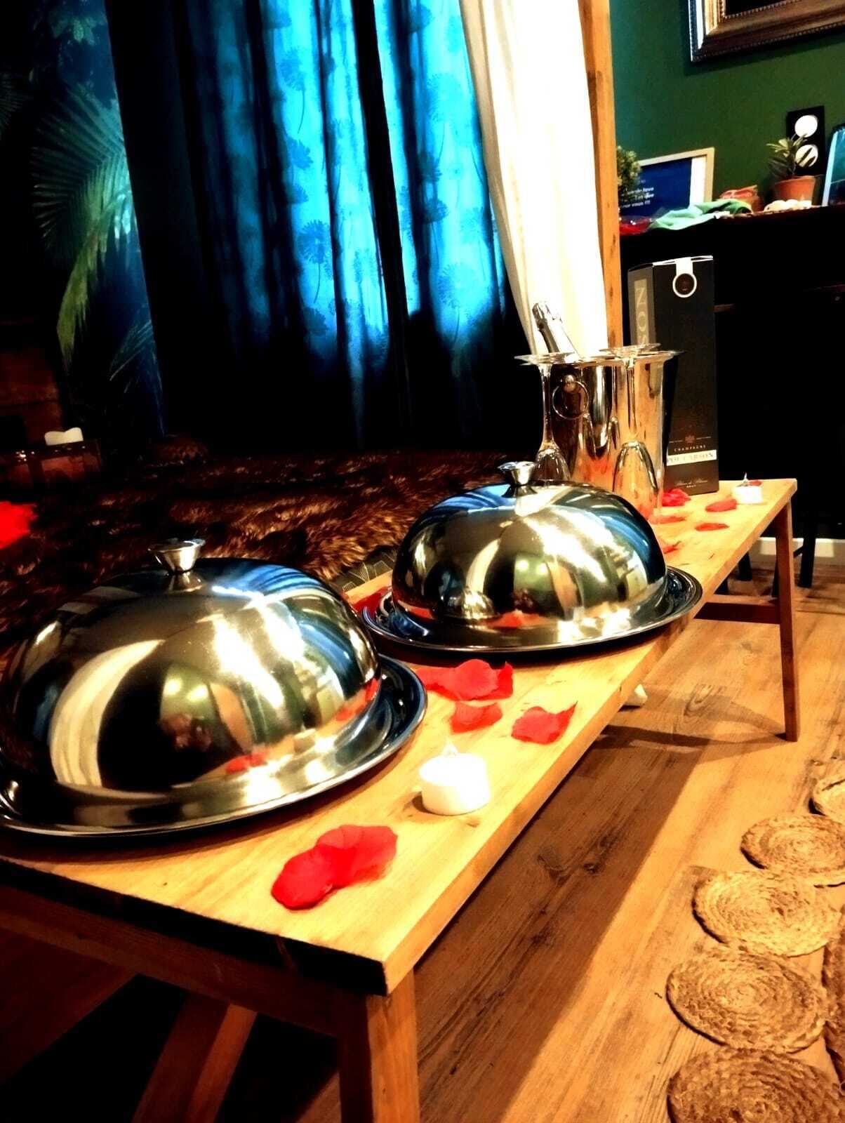 A wooden table with two covered dishes and a candle, set against a backdrop of blue curtains and a green wall.