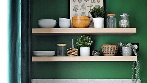 Una cocina con estantes de madera, un lavamanos blanco, una cafetera y un refrigerador antiguo.