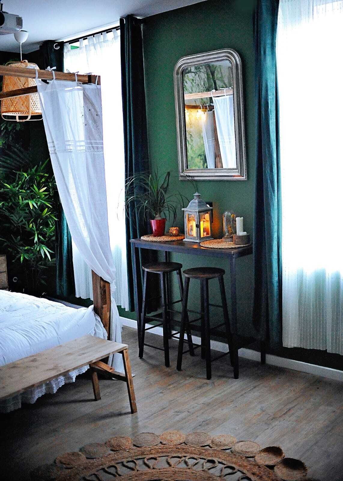Quarto com cama, escrivaninha com bancos, espelho e planta em vaso.
