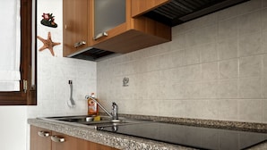 A modern kitchen with wooden cabinets, a granite countertop, a stainless steel sink, and a built-in oven. - Apartment With Pool Near the Beach (Rosolina)