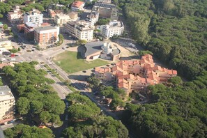 An aerial view of a residential area with a prominent building featuring a circular central structure, surrounded by lush greenery and other residential buildings. - Apartment With Pool Near the Beach (Rosolina)