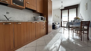 A modern kitchen with wooden cabinets, a microwave, and a dining area with a table and chairs. - Apartment With Pool Near the Beach (Rosolina)