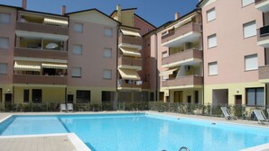 A swimming pool surrounded by multi-story residential buildings with balconies and outdoor seating. - Apartment With Pool Near the Beach (Rosolina)