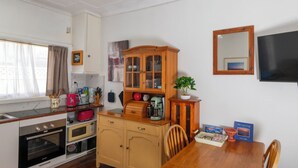 A compact kitchen with a wooden table, cabinets, and a television. - Unit 1 - A welcoming and cosy unit, near Wanda beach and Cronulla Golf Course (Cronulla)